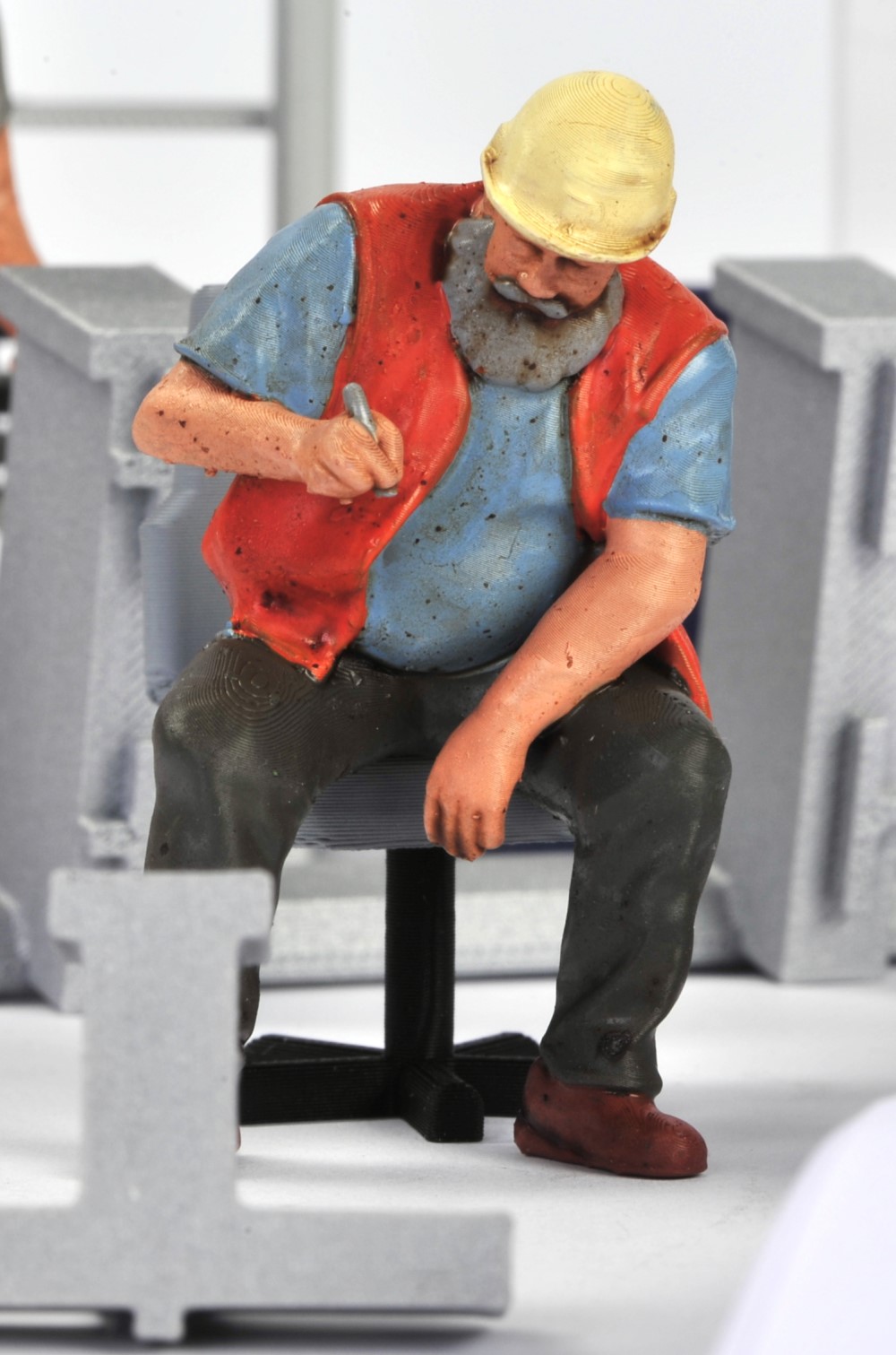 Der sitzende RhB Bahnarbeiter ist ebenfalls mit gelbem Schutzhelm, oranger Warnweste und blauem Shirt mit schwarzer Hose von Volker Bauer figurendesign gefertigt worden. 