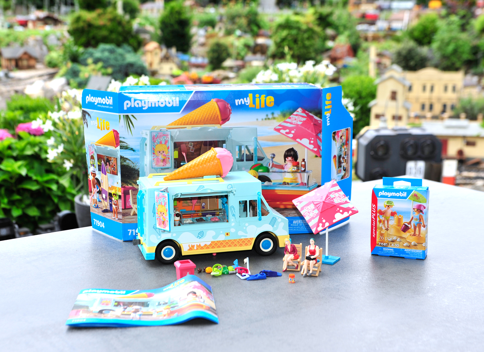 Für den Zusammenbau sind gut 45 Minuten vergangen. Die Playmobilfiguren sind noch im Beutel verpackt, da der Eiswagen ja auf die Gartenbahnanlage platziert werden soll. Tauchermasken, Schwimmflossen und weitere Kleinteile sind im Wageninneren zu verstauen. Auch das Stand-Up Paddelboot mit dem Paddel ist im Wagen platziert. Die Eistheke kann bei Bedarf auch außerhalb des Wagens aufgestellt werden. So wie es auf dem Verkaufskarton zu sehen ist. Auf die Stühle habe ich zwei sitzende Figuren aus dem Gartenbahnsortiment platziert. Die Größe des Wagens ist mit 12 cm Breite (umgerechnet auf 1:22,5 - 2,70 Meter), 26 cm Länge (umgerechnet auf 1:22,5 - 5,85 Meter) und 14 cm Höhe (umgerechnet auf 1:22,5 - 3,15) für die Gartenbahn geeignet. Ein LKW darf die Höhe von 4 Metern in Deutschland nur mit Sondergenehmigung überschreiten.