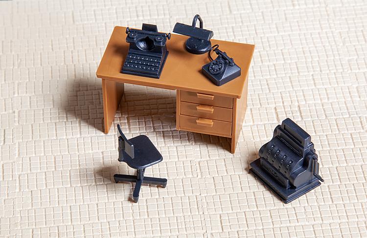 Broschreibtisch mit Drehstuhl, Schreibmaschine, Tischlampe und Telefon.