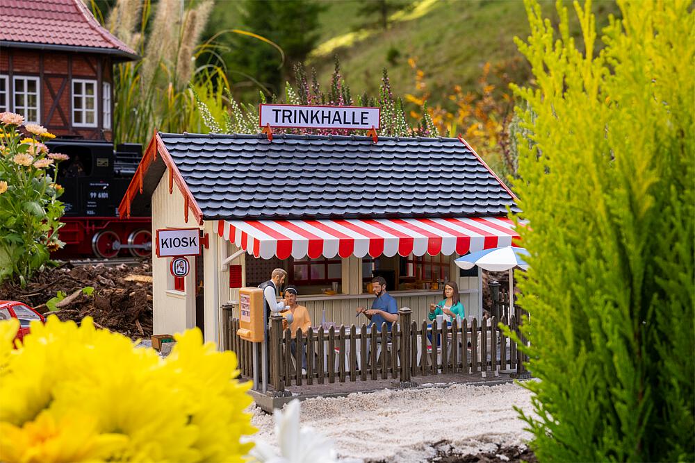 Pola Art. Nr. 331111 - Geselliger Treffpunkt f�r eine kleine Pause! Das Modell �berzeugt durch seine Gestaltung mit heller Holzverkleidung, einem klassischen Satteldach mit dunklen Dachziegeln und einer markanten rot-wei�en Markise �ber den gro�en Verkaufsfenstern. Durch die offene Theke blickt man direkt auf Flaschen, Gl�ser und kleine Snacks. Vor dem Kiosk sorgt der eingez�unte Biergarten mit wei�en Gartenst�hlen, Tischen und blau-wei�em Sonnenschirm f�r gem�tliche Atmosph�re. Liebevolle Details wie Getr�nkekisten, ein Zigarettenautomat und nostalgische Reklameschilder runden die Szene stimmungsvoll ab!