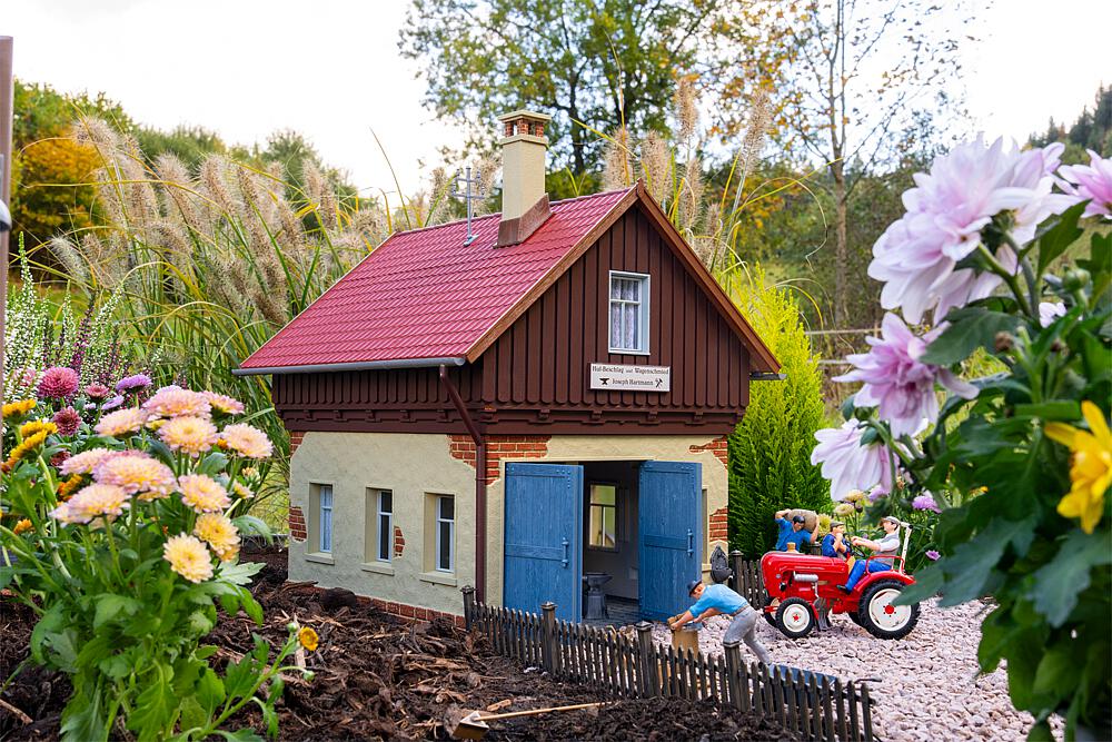 POLA Art. Nr. 331179 - Hier wird noch von Hand gearbeitet! Mit diesem Modell einer historischen Dorfschmiede holen Sie das traditionelle Handwerk vergangener Zeiten auf Ihre Gartenbahn-Anlage. Die Schmiede besticht durch massives Mauerwerk im Erdgeschoss, kombiniert mit einem holzverkleideten Giebelbereich und einem klassischen Satteldach mit roten Dachziegeln, die der Schmiede ihren einzigartigen Charme verleihen. Die gro�en blauen Doppeltore gew�hren Einblick in die detailreich eingerichtete Werkstatt. Umfangreich ausgestattet ist die Schmiede mit einer Esse, einem Amboss, zahlreichen Werkzeugen, einer Werkbank, einem Wagenrad sowie 