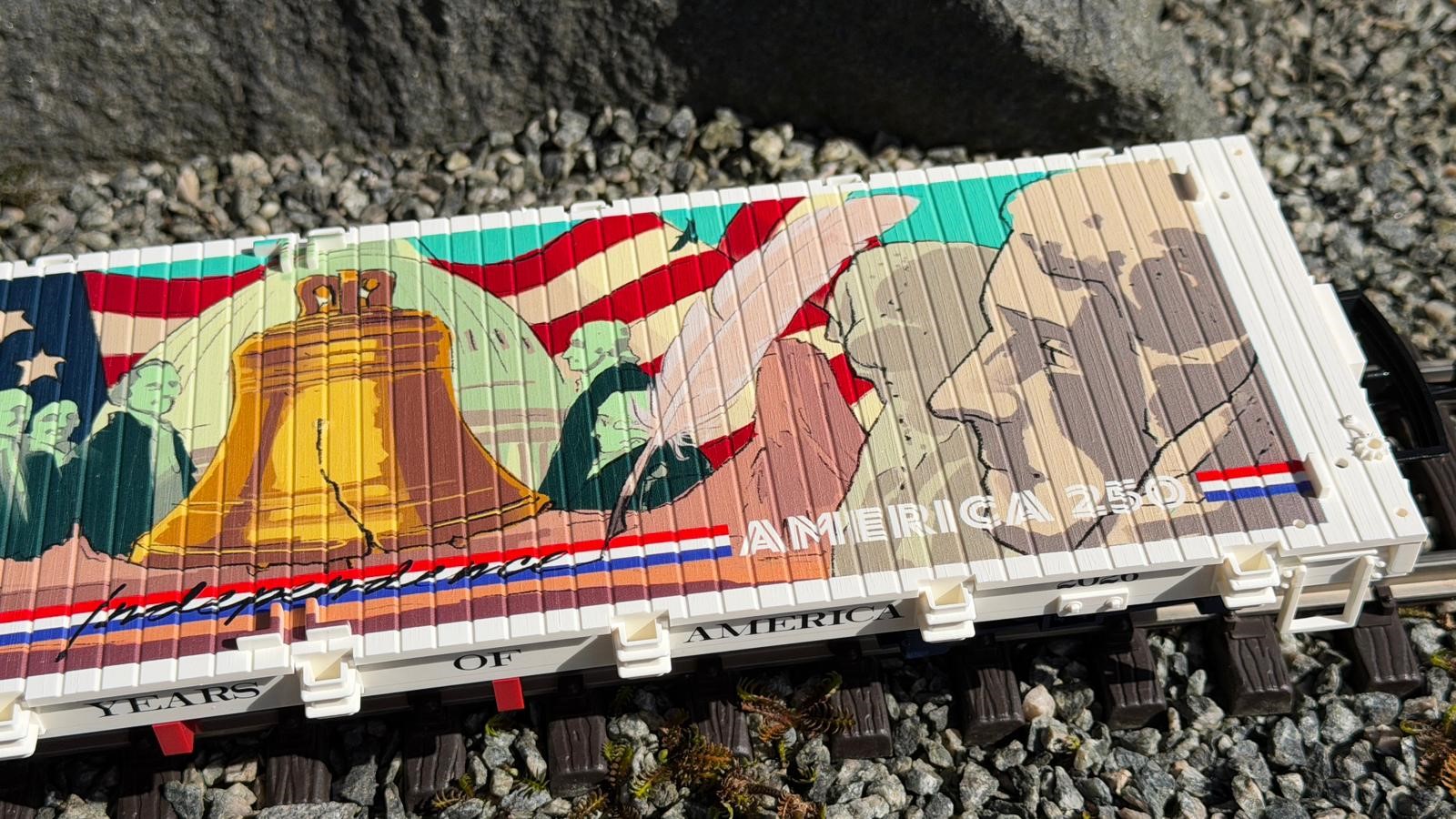 Die aufwendige Bedruckung des Wagenbodens des Art. 40598 zeigt auf der Mitte und der rechten Seite die Liberty Bell vor dem Dom des Capitols, auf dem rot-wei�-blauen Streifen den Schriftzug "Independence" (Unabh�ngikeit) mit der Schreibfeder sowie AMERICA 250 und weitere Personen. 