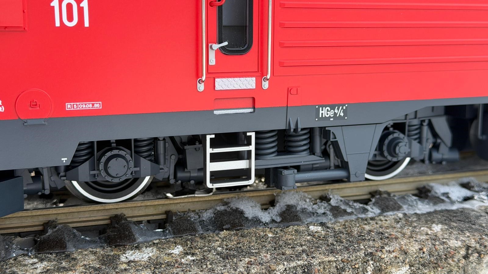 Detailaufnahme vom Einstieg in die HGe 4/4 II der FO Nr. 101 - Art. Nr. 23103 von LGB - Herbstneuheit 2025. Die Aufstiegsleiter sowie das Kantenblech unterhalb der T�re sind sehr gut nachgebildet und setzen durch die silberne Lackierung einen tollen Akzent an die Lok. Das Typenschild ist ebenfalls Originalgetreu angebracht. Als Revisionsdatum ist die Nr. 5 mit Datum 9.8.85 aufgedruckt. Somit ist diese Lok schon lange im Einsatz. 
