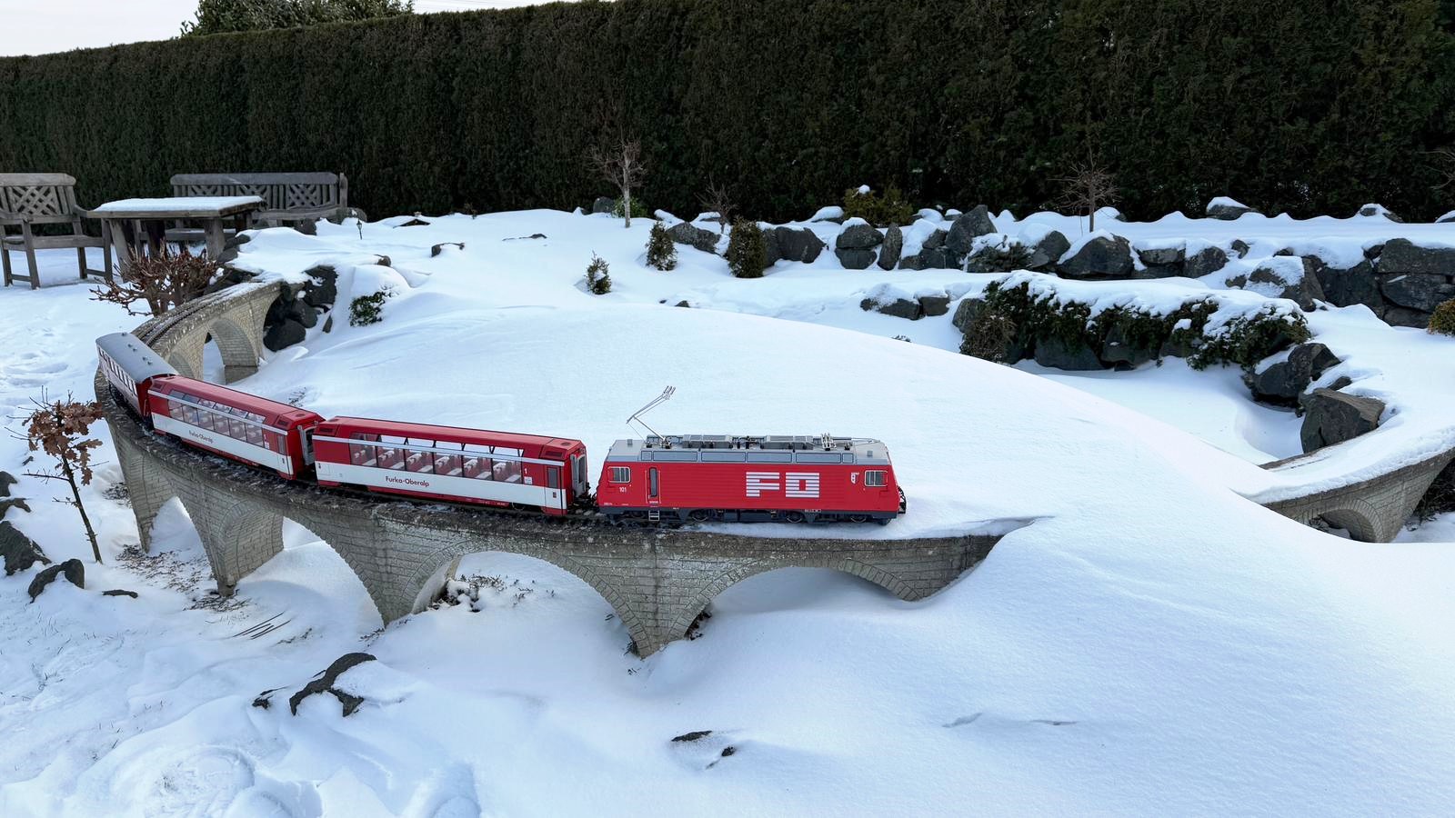 Das Modell der HGe 4/4 II der FO Nr. 101 - Art. Nr. 23103 von LGB - Herbstneuheit 2025 - mit dem kleinen Glacier Express auf der Gartenbahn im Norden mit Schneeverwehung. Es wird nun auf die Schneefr�se gewartet. 