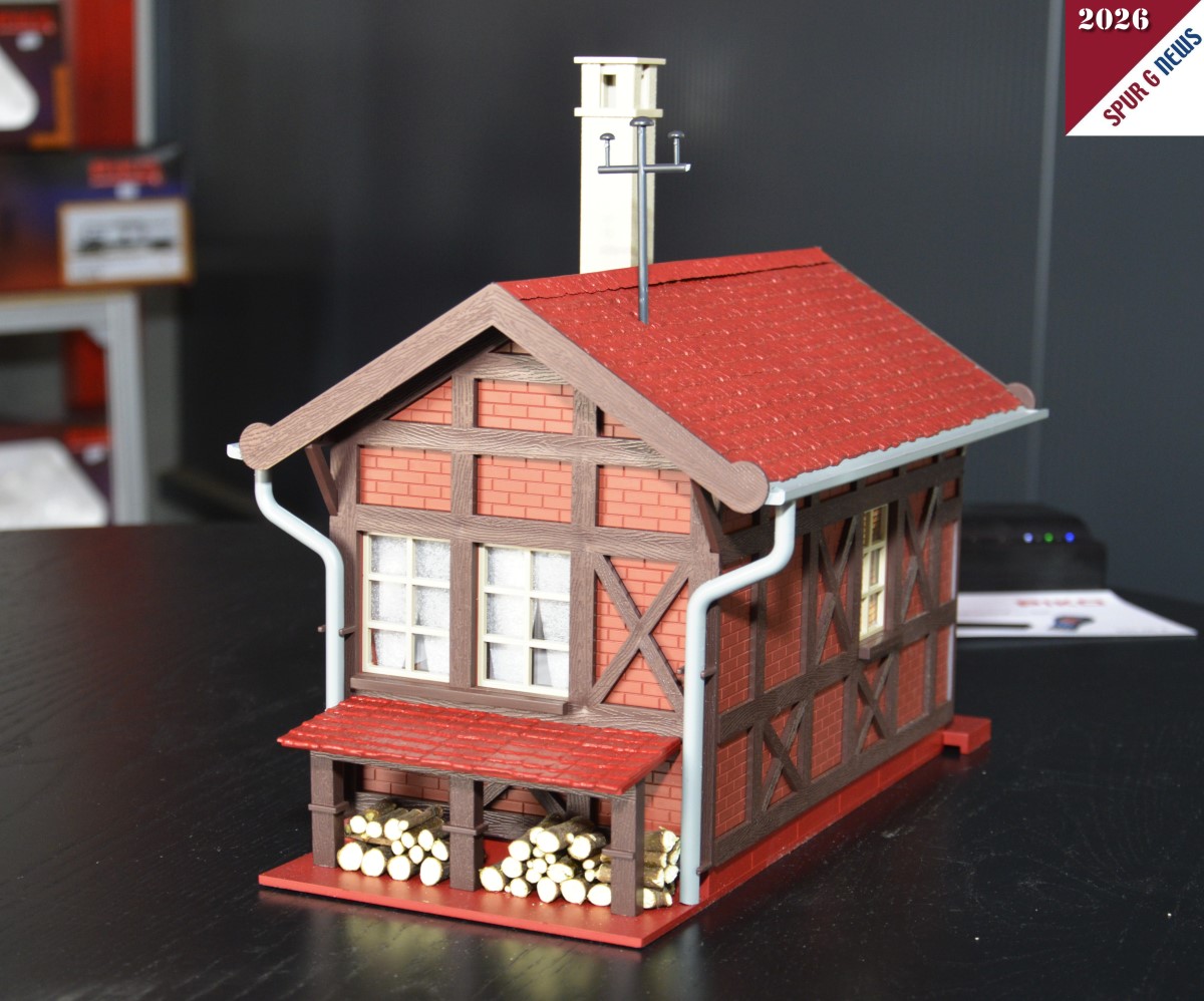 Das Bahnw�rterhaus - Art. Nr. 65002 - konnten wir auf dem Pr�sentiertisch fotografieren. Link der Eingang des Hauses und rechts der Hinterhof mit dem gestapelten Holz unter der kleinen �berdachung. Sicherlich ragt der Kamin im Vorbild des Bahnw�rterhauses auch so in die H�he. Im Prospekt ist das Fachwerk wei� abgebildet. Hier beim Start in die Gartenbahnsaison sind es Klinkersteine die zwischen den aufgesetzten Balken eingebaut sind. Auch die Dachrinnen sind hier im Muster grau dargestellt. Im Prospekt gr�n. Wir werden erneut dar�ber berichten. 